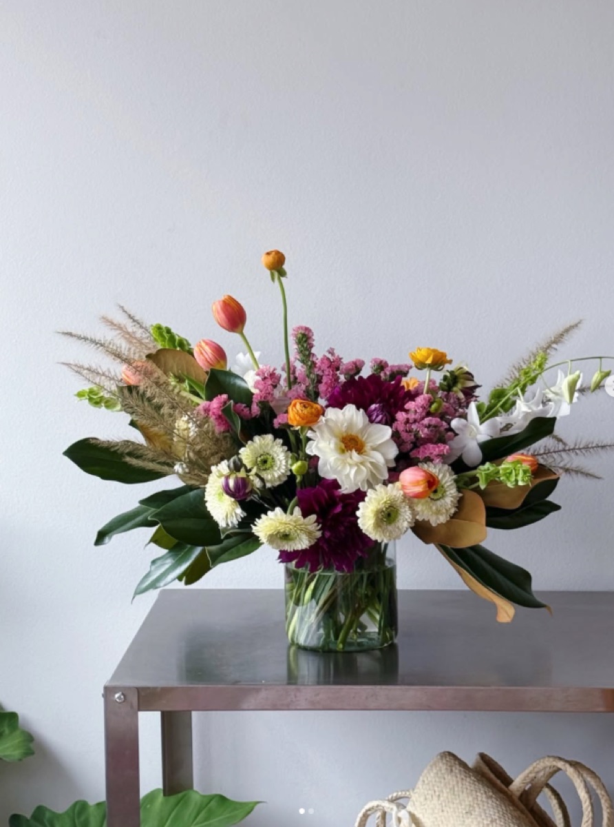 Vaso de vidro com arranjo grande de rosas, dálias, cosmos e lisianthus em mesa branca